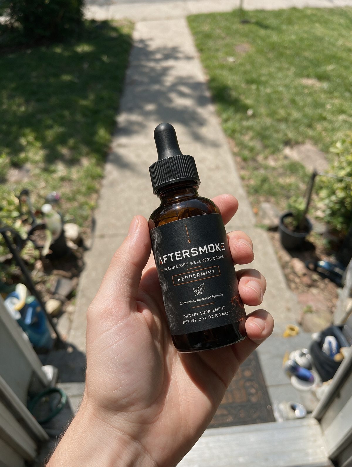 AFTERSMOKE bottle held in hand outside on a sunny sidewalk
